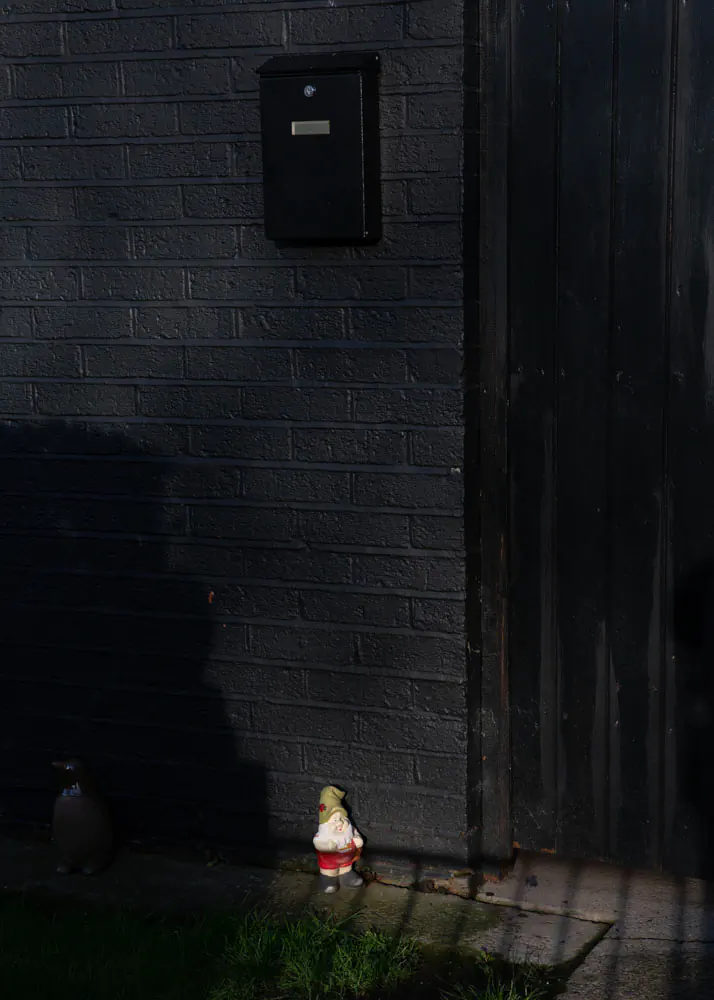 Small gnome garden ornament against black wall and post box