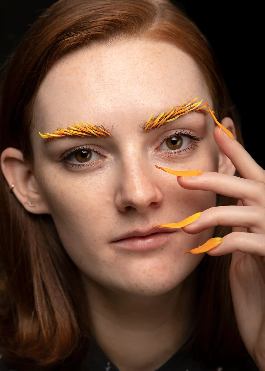 Close up portrait of young woman with orange dragon scale flower petals on eyebrows and nails