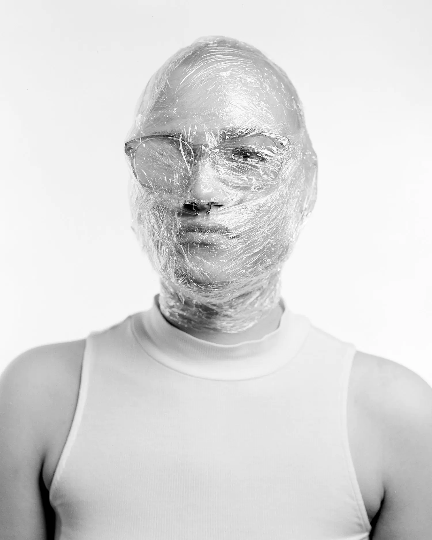 Large format portrait of young bald woman with head wrapped in clingfilm and steamed up glasses