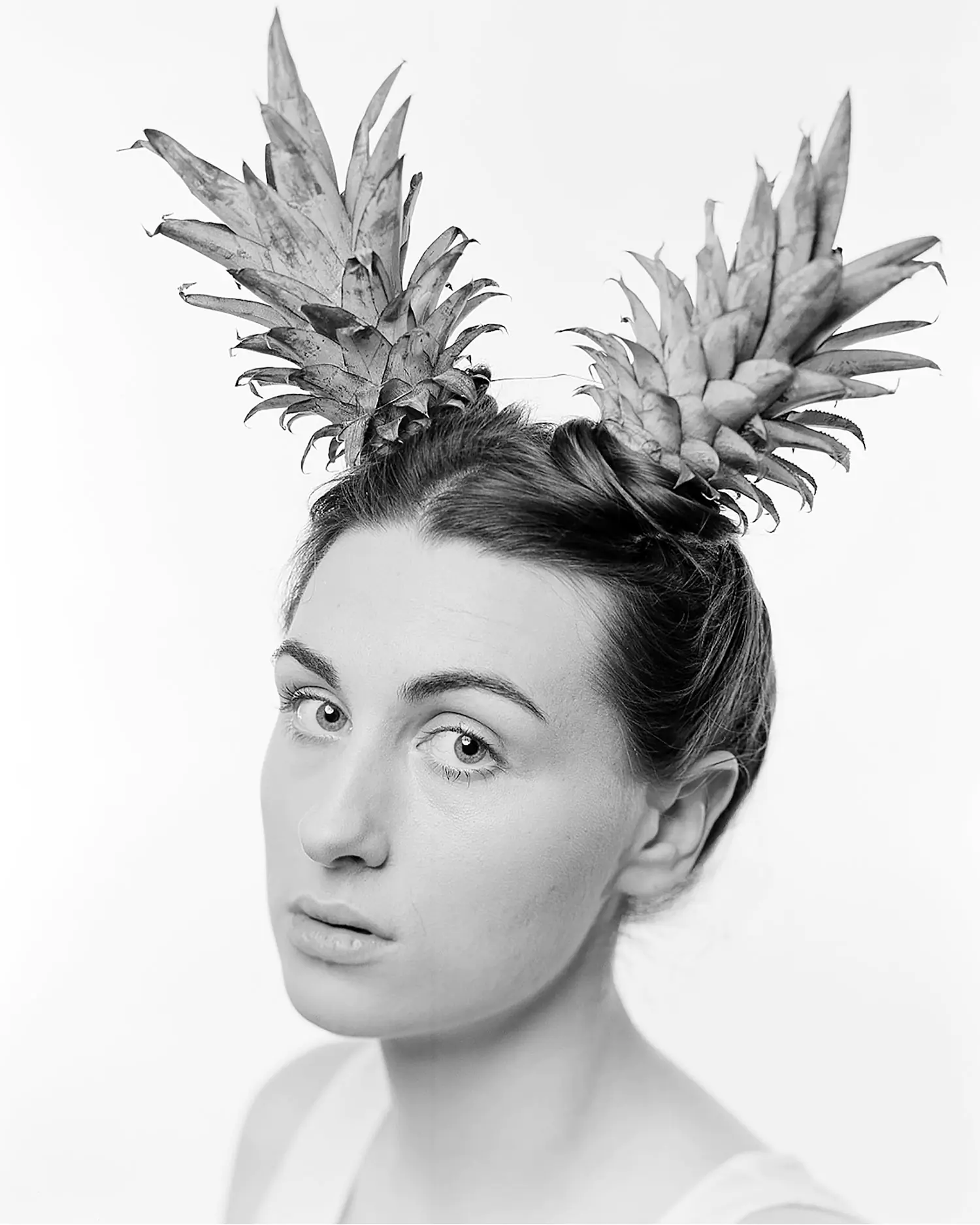 Large format portrait of young woman with pineapples on head