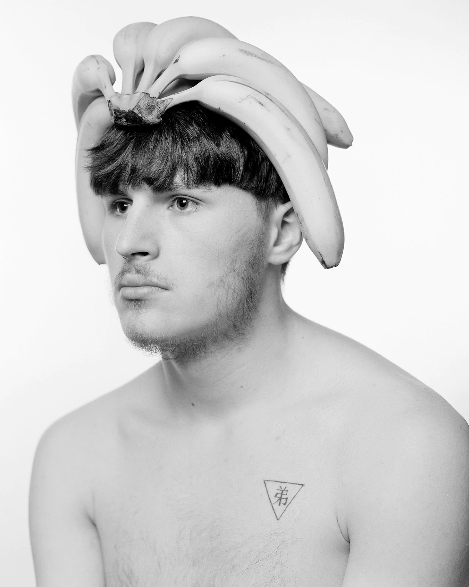 Large format black and white portrait of young man wearing bananas on head