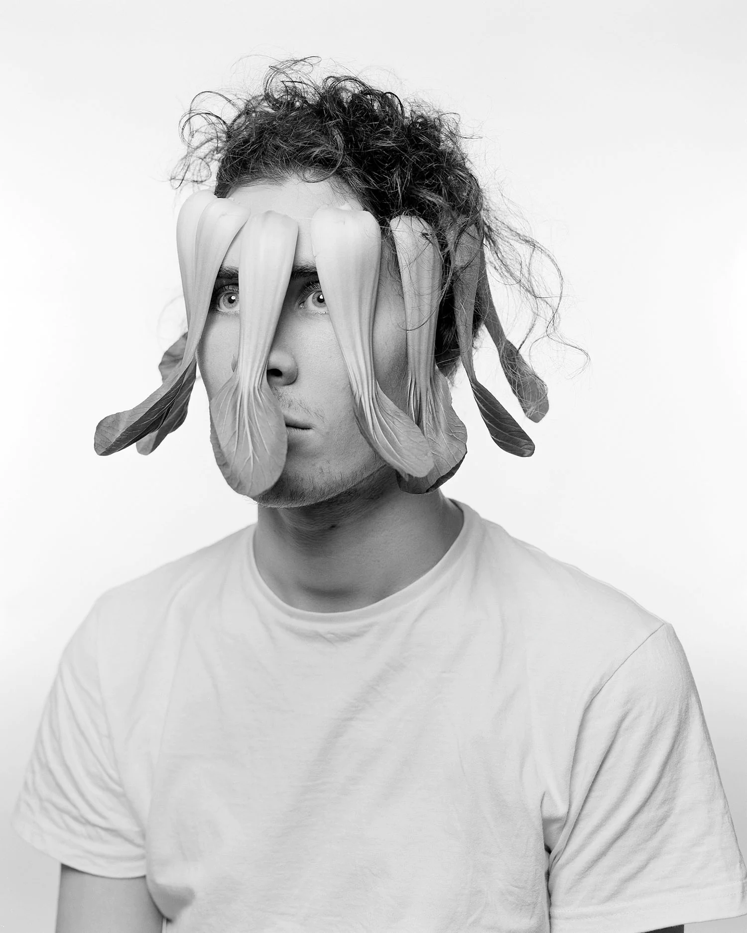 Large format black and white portrait of young man with pak choi as face shield
